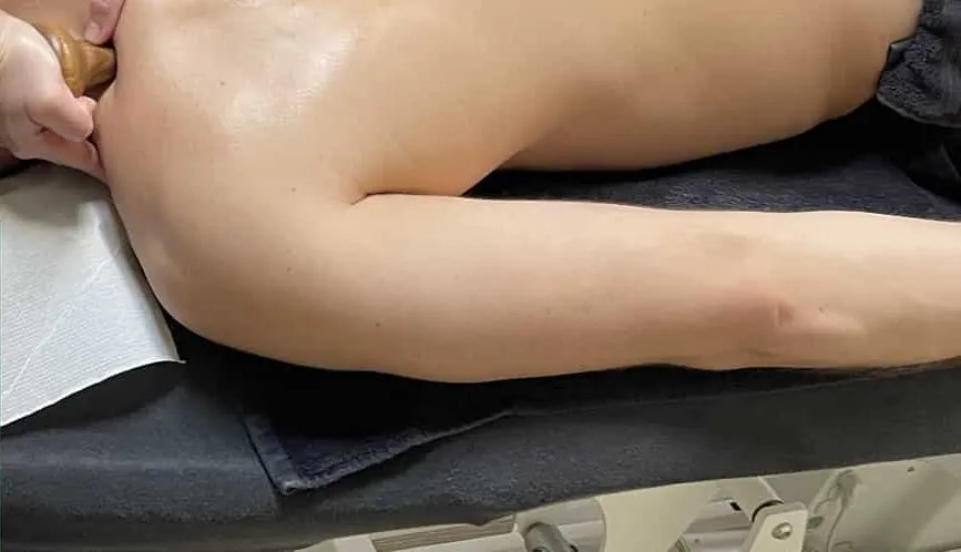 Masseuse behandelt de schouder van een cliënt op de behandeltafel